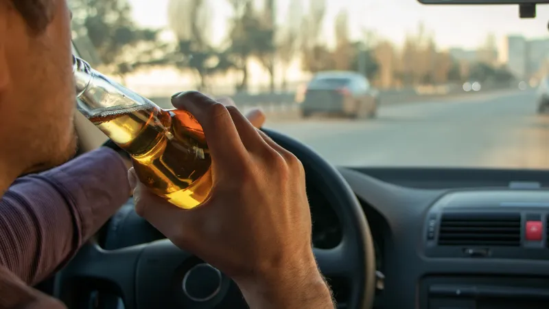 A man drinking alcohol while driving. Drunk driving concept.