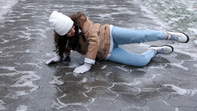 Young woman fallen on slippery icy pavement outdoors