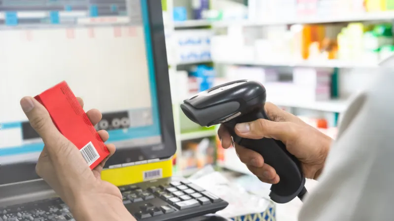 Pharmacist scanning price on a red medicine box with barcode reader in pharmacy store