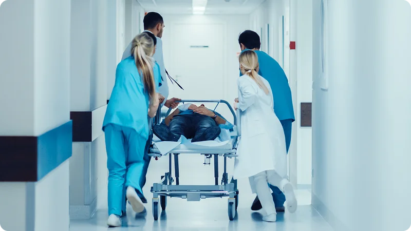Four medical professionals in a hospital hallway, urgently pushing a patient on a gurney.