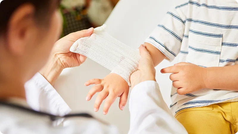 A healthcare professional bandaging a young child’s injured hand.