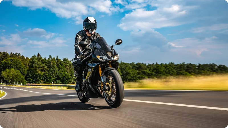 A motorcyclist riding a black sport bike on a winding road, with a helmet and full riding gear.