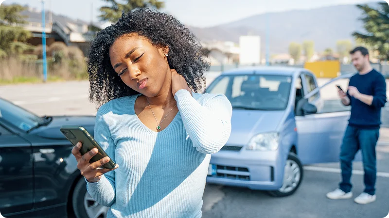 A young Black woman with her hand on her neck, looking at her phone with a pained expression.