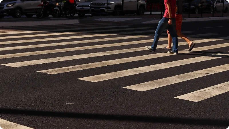 A man and a woman walking across a black asphalt road on a white-striped crosswalk.