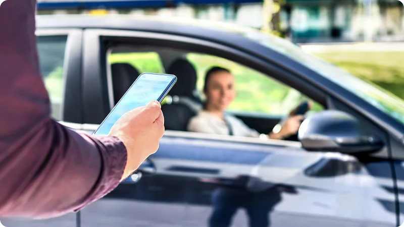 A woman in the driver's seat of the car is looking towards the person's holding a smartphone outside.