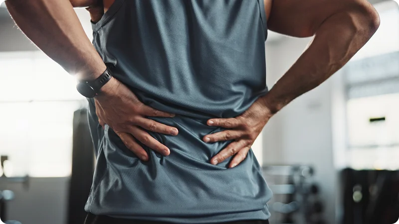 A man is holding his lower back with both hands, showing he is experiencing back pain or has a spinal injury.